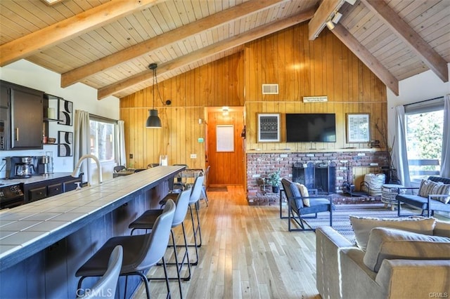 kitchen featuring beam ceiling, light hardwood / wood-style flooring, tile countertops, wood walls, and decorative light fixtures