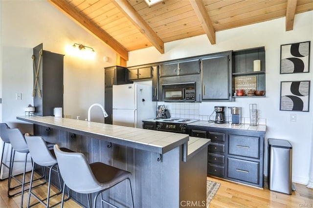 kitchen with a kitchen breakfast bar, tile countertops, light hardwood / wood-style floors, white appliances, and vaulted ceiling with skylight