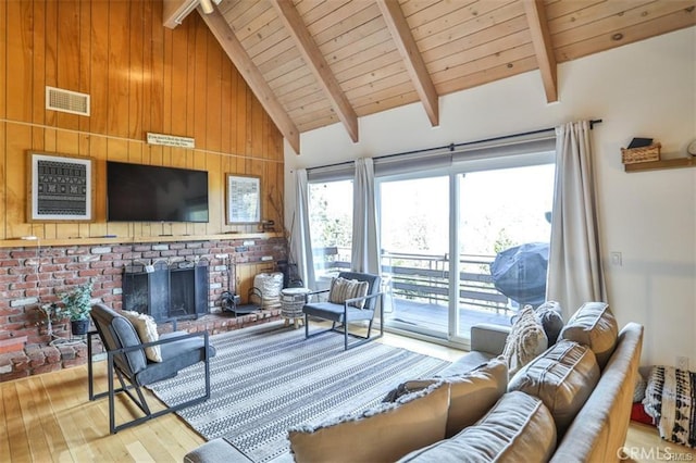 living room with beam ceiling, light wood-type flooring, a wealth of natural light, and a brick fireplace