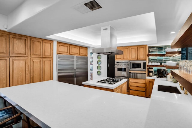 kitchen featuring island range hood, built in appliances, a raised ceiling, and a kitchen bar