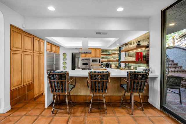 kitchen with stainless steel appliances, a kitchen breakfast bar, a raised ceiling, decorative backsplash, and kitchen peninsula