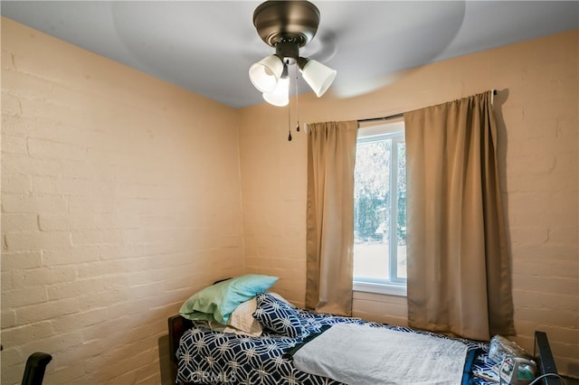 bedroom with ceiling fan and brick wall