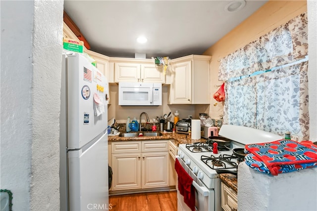 kitchen with sink, white appliances, cream cabinets, dark stone countertops, and light wood-type flooring