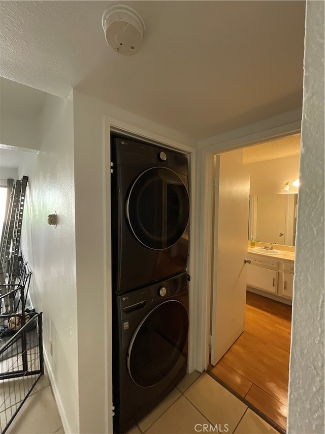 laundry area with sink, stacked washer / dryer, light hardwood / wood-style floors, and a textured ceiling