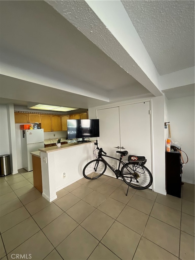 kitchen with light tile patterned flooring, kitchen peninsula, white fridge, and a textured ceiling