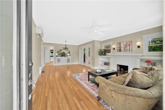 living room with ceiling fan with notable chandelier, french doors, a wall unit AC, hardwood / wood-style flooring, and crown molding