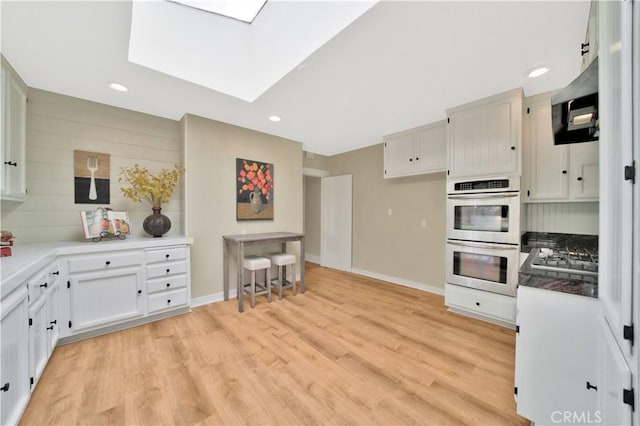 kitchen with stainless steel gas stovetop, light hardwood / wood-style flooring, a skylight, white cabinets, and double oven