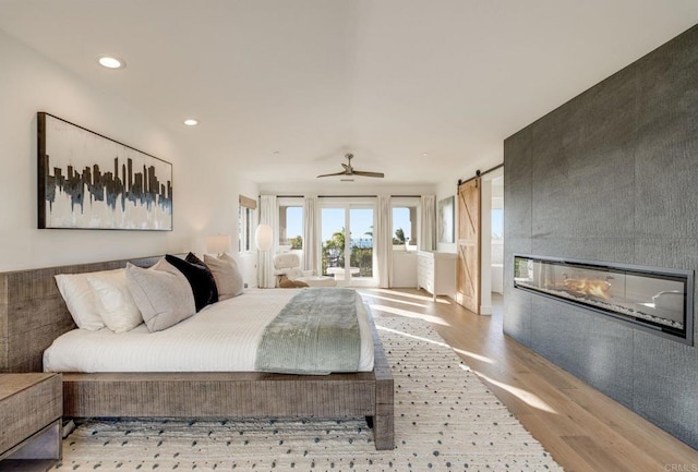 bedroom featuring a barn door, a tiled fireplace, and light wood-type flooring