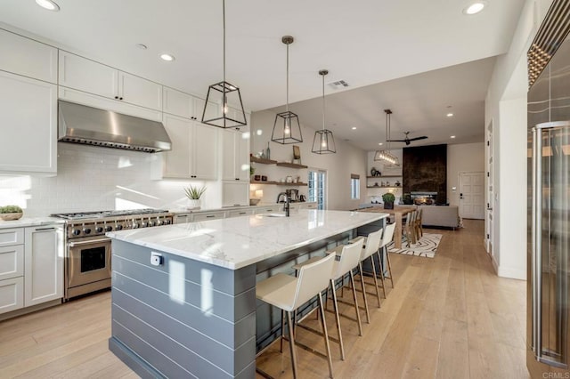 kitchen featuring a center island with sink, white cabinetry, wall chimney range hood, and high end stainless steel range