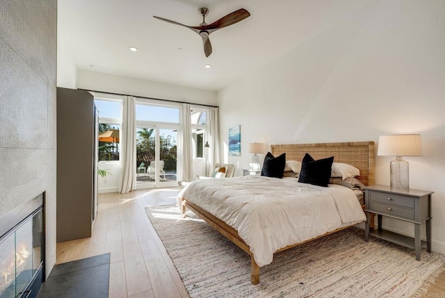 bedroom with ceiling fan, a large fireplace, light wood-type flooring, and access to outside