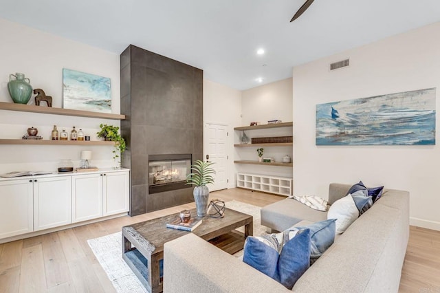 living room with ceiling fan, a tile fireplace, and light hardwood / wood-style flooring