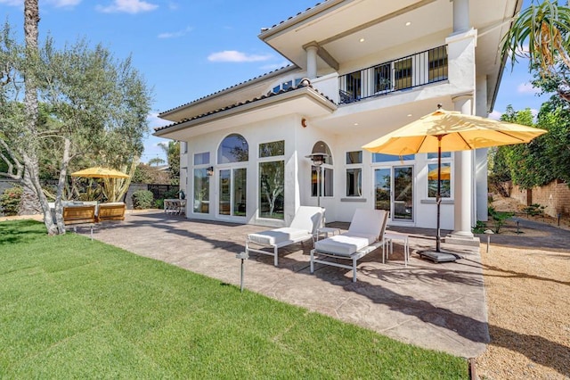 back of property with a balcony, a patio, and a lawn