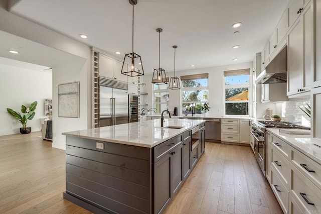 kitchen featuring high quality appliances, white cabinetry, hanging light fixtures, a large island, and light stone counters