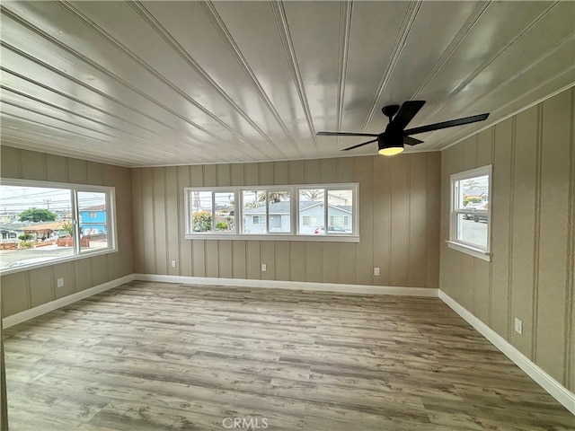 spare room featuring ceiling fan, light hardwood / wood-style flooring, and wood walls