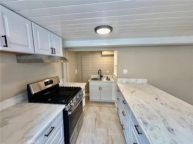 kitchen with light stone countertops, stainless steel gas range, white cabinetry, and sink