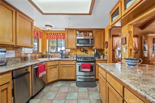 kitchen with a textured ceiling, beam ceiling, stainless steel appliances, and light stone counters