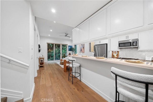 kitchen with a kitchen breakfast bar, ceiling fan, light wood-type flooring, appliances with stainless steel finishes, and white cabinetry