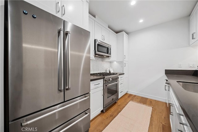 kitchen with high end appliances, white cabinets, sink, light wood-type flooring, and tasteful backsplash