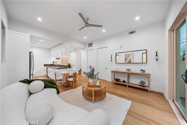 living room with light wood-type flooring, ceiling fan, and sink