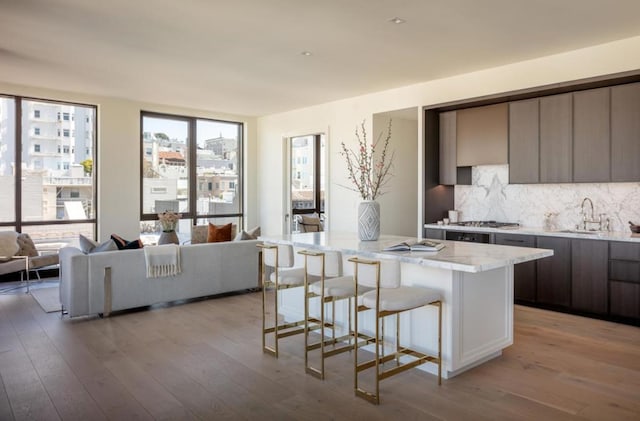 kitchen featuring a breakfast bar area, backsplash, a kitchen island, light stone counters, and sink