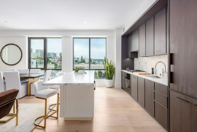 kitchen with light hardwood / wood-style floors, backsplash, sink, light stone countertops, and a center island