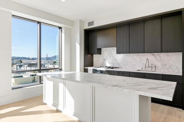 kitchen featuring tasteful backsplash, a kitchen island, light hardwood / wood-style floors, sink, and light stone countertops