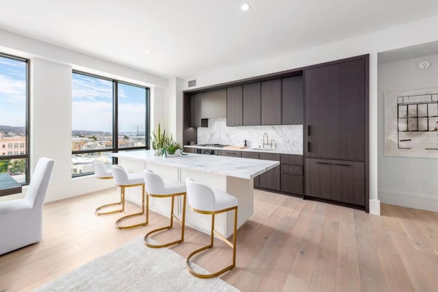 kitchen with light hardwood / wood-style floors, backsplash, sink, dark brown cabinets, and a center island