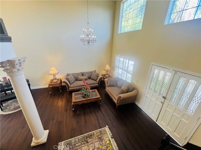 living room with decorative columns, a towering ceiling, dark hardwood / wood-style floors, and a notable chandelier