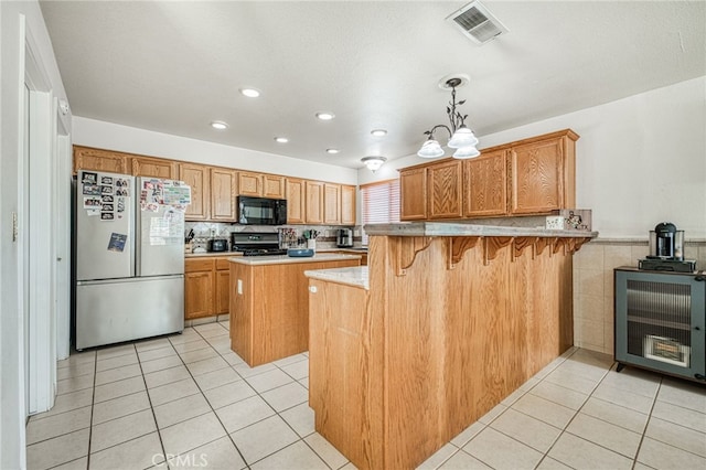 kitchen with black appliances, hanging light fixtures, light tile patterned floors, kitchen peninsula, and a breakfast bar area