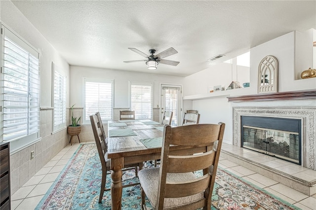 dining room featuring light tile patterned floors, a textured ceiling, ceiling fan, and a tiled fireplace