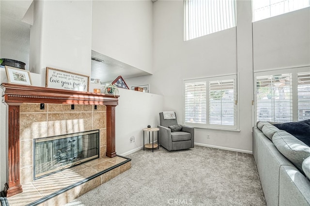 living room with carpet flooring, a towering ceiling, and a tiled fireplace