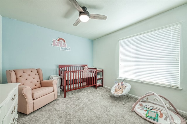 carpeted bedroom featuring ceiling fan and a crib