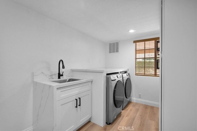 laundry area featuring washer and clothes dryer, cabinets, light wood-type flooring, and sink