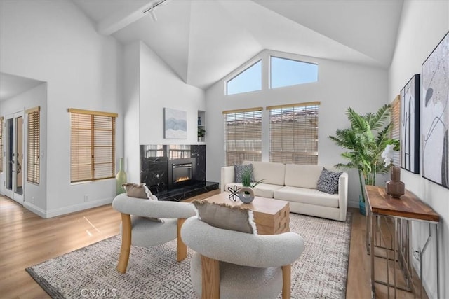 living room featuring light hardwood / wood-style floors, a premium fireplace, rail lighting, and high vaulted ceiling