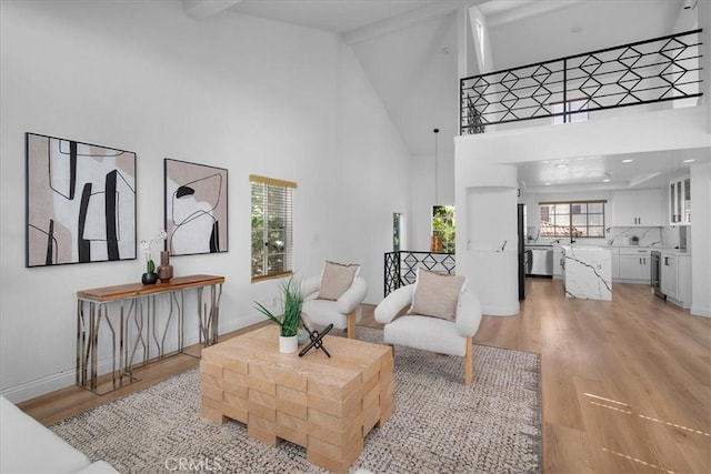 living room with beam ceiling, light wood-type flooring, and high vaulted ceiling