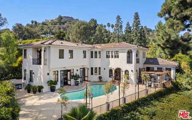 back of house with a fenced in pool, a pergola, and a patio