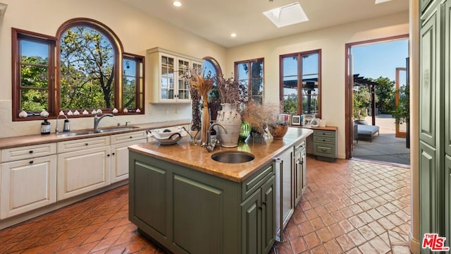 kitchen with sink, white cabinets, a center island with sink, and a skylight