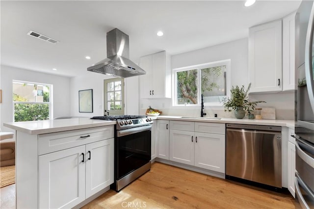 kitchen featuring appliances with stainless steel finishes, island range hood, white cabinetry, sink, and kitchen peninsula