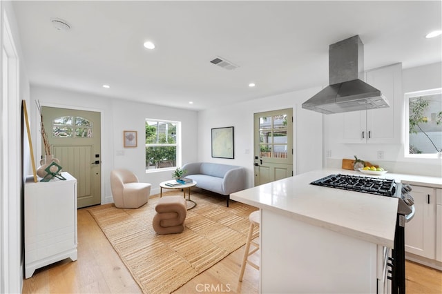 kitchen featuring range with gas stovetop, light hardwood / wood-style floors, range hood, white cabinets, and a kitchen bar