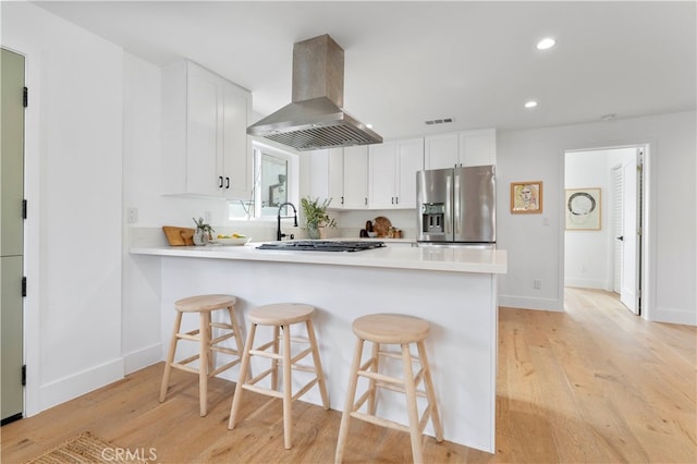 kitchen with light hardwood / wood-style floors, a breakfast bar, white cabinets, stainless steel appliances, and ventilation hood