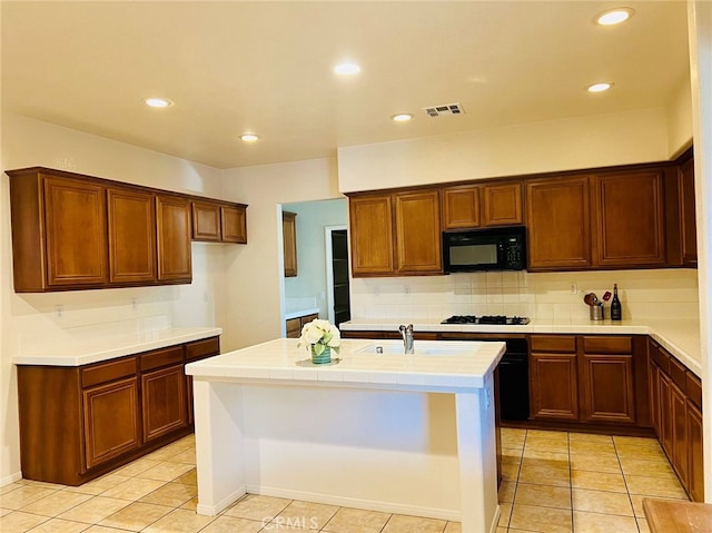 kitchen featuring decorative backsplash, light tile patterned flooring, white gas stovetop, a center island with sink, and sink