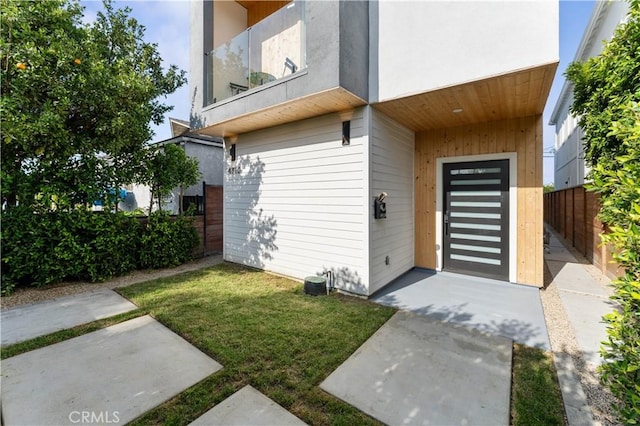 view of exterior entry with a yard and a balcony