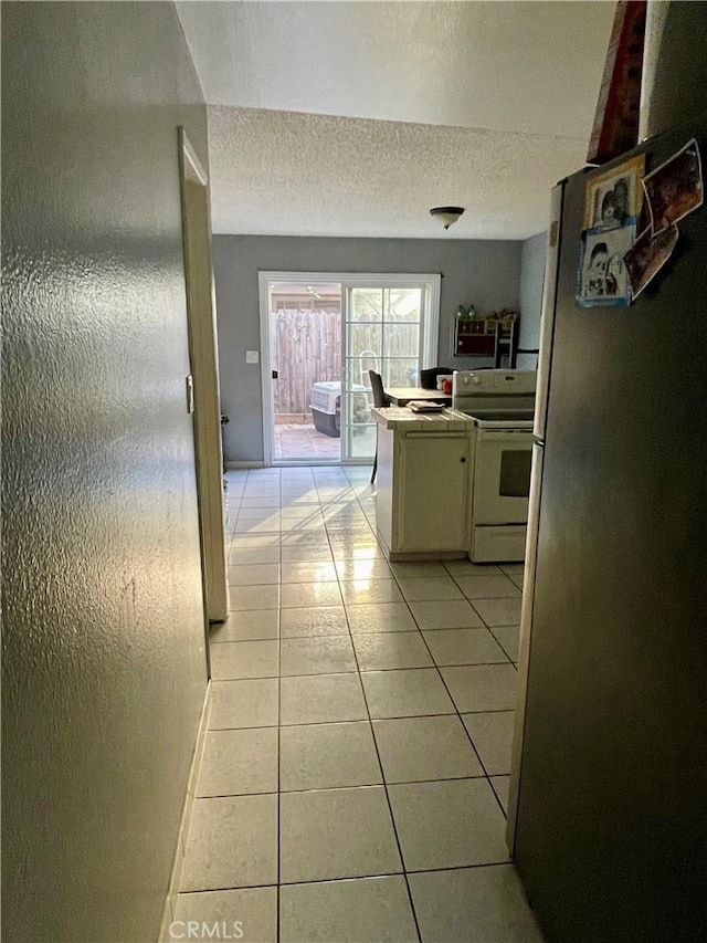 kitchen with stainless steel fridge, light tile patterned flooring, white range oven, and a textured ceiling