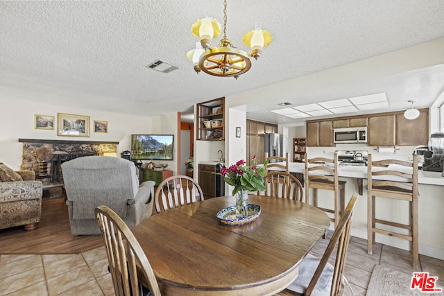 dining area with a fireplace, light tile patterned flooring, a textured ceiling, and an inviting chandelier