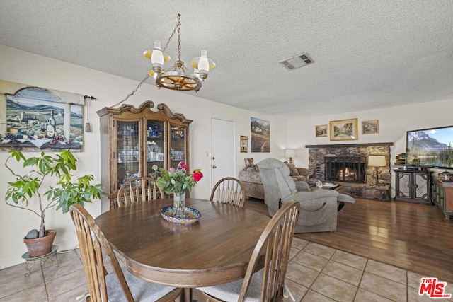 dining space featuring light tile patterned floors, a fireplace, an inviting chandelier, and a textured ceiling