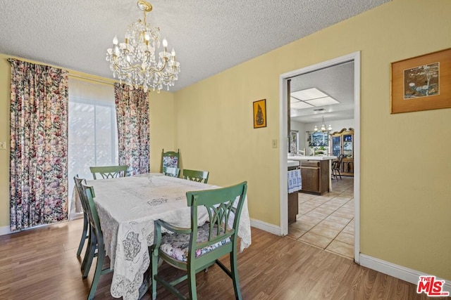 dining space with light wood-type flooring, a textured ceiling, plenty of natural light, and a notable chandelier