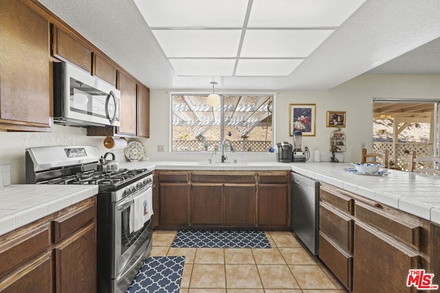 kitchen featuring decorative light fixtures, sink, stainless steel appliances, tile counters, and light tile patterned floors