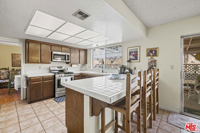 kitchen featuring light tile patterned floors, a textured ceiling, appliances with stainless steel finishes, and tile countertops