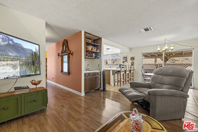 living room featuring a textured ceiling, a chandelier, wood-type flooring, and sink