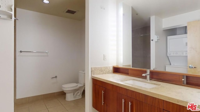 bathroom featuring tile patterned flooring, vanity, stacked washing maching and dryer, and toilet